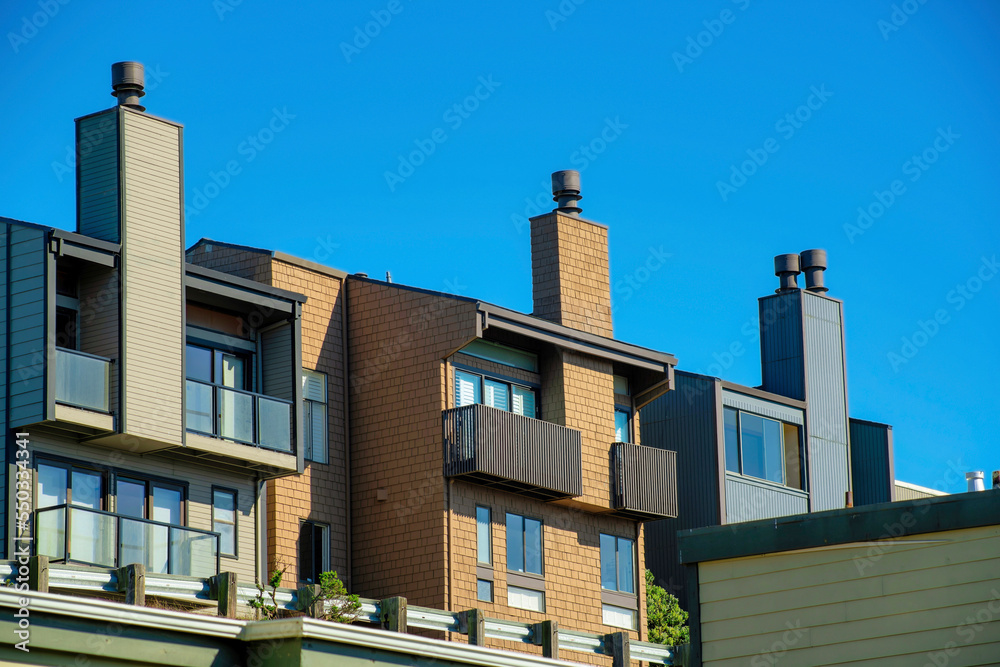 Row of modern houses or apartment buildings with chimneys and wooden exteriors with clear blue and white sky background