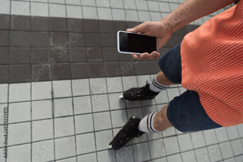 Fototapeta Naklejka Na Ścianę i Meble -  Top view of roller skater holding smartphone with blank screen outdoors.