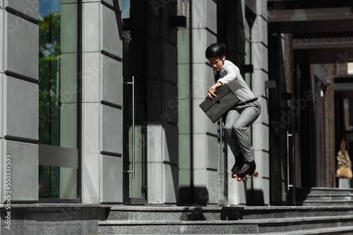 Businessman in roller skates jumping and holding briefcase while riding on urban street.