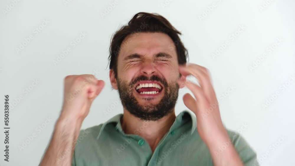Handsome young bearded man looks at camera with uncertainty and expectation, then suddenly rejoices and clenches his fists from what he saw or good news, smiling with a cheerful beautiful toothy smile Handsome young bearded man looks at camera with uncertainty and expectation, then suddenly rejoices and clenches his fists from what he saw or good news, smiling with a cheerful beautiful toothy smile