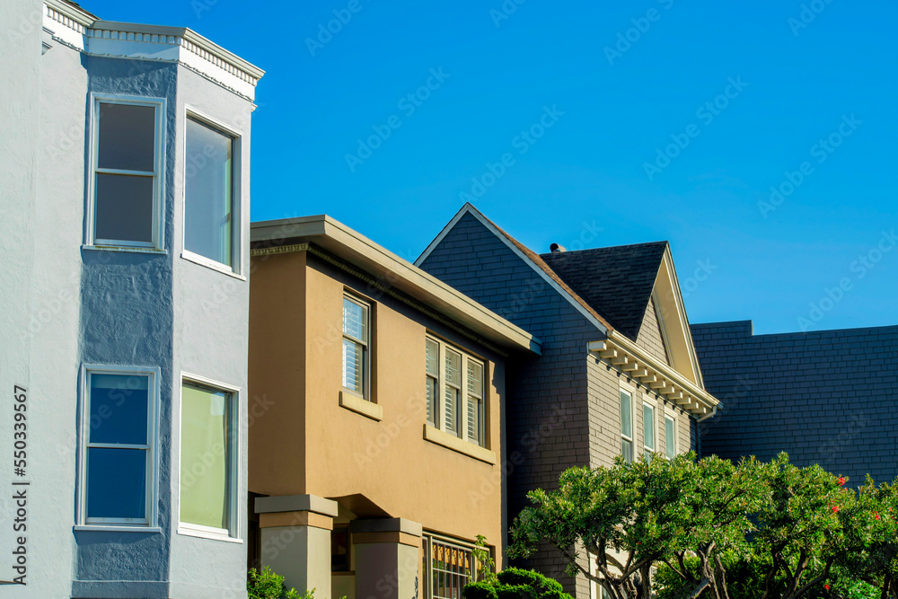 Row of decorative houses with visible windows and brown and blue and yellow exterior with front yard trees in the neighborhoods
