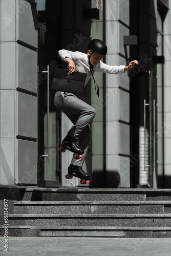 Young businessman in roller skates jumping and holding briefcase on urban street.