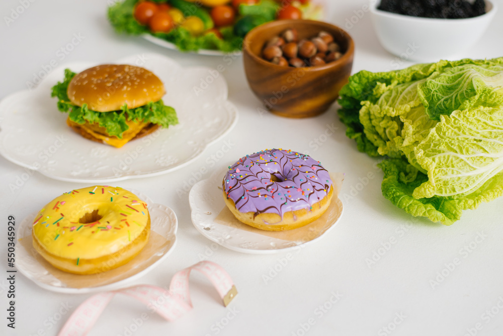 Healthy or unhealthy food. Conceptual photo of healthy and unhealthy food with measuring tape. Fruits and vegetables vs donuts, sweets and burgers Healthy or unhealthy food. Conceptual photo of healthy and unhealthy food with measuring tape. Fruits and vegetables vs donuts, sweets and burgers