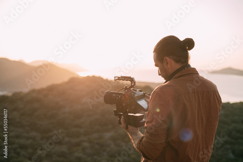 A young Caucasian man with a professional camera in his hands on a mountain by the sea.