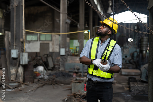 African American male engineer in vest and helmet safety operating control overhead crane for moving heavy metal at factory. Professional technicians in industrial machinery