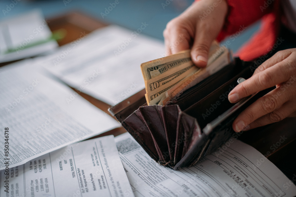 Naklejka premium The hands of an elderly woman with a purse with money and a lot of utility bills.