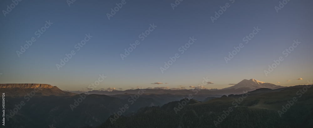 Panorama of the mountain landscape of Mount Elbrus with snow and glaciers at sunset lighting, cloudy sunset sky