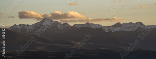 Panorama of a mountain range with peaks with snow and ice at sunset with a cloudy sky, mountain rocky peaks in autumn © Denis