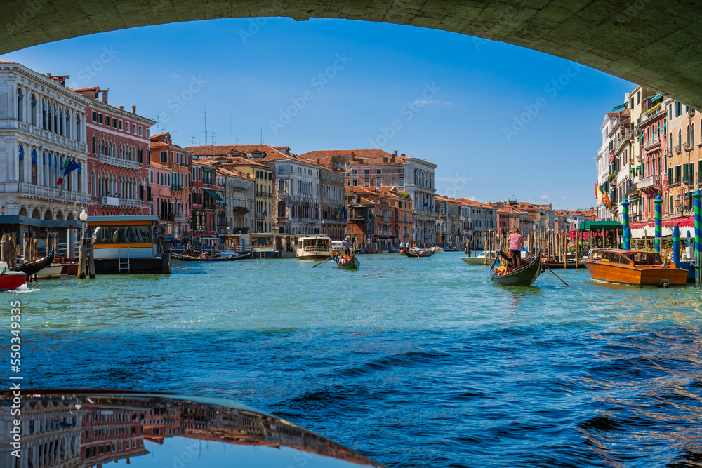 Obraz premium Boats and gondolas with tourists while traveling through the canals of Venice in Italy in the summer near the Rialto Bridge on the Grand Canal. Ancient architecture and sights in Italian Venice