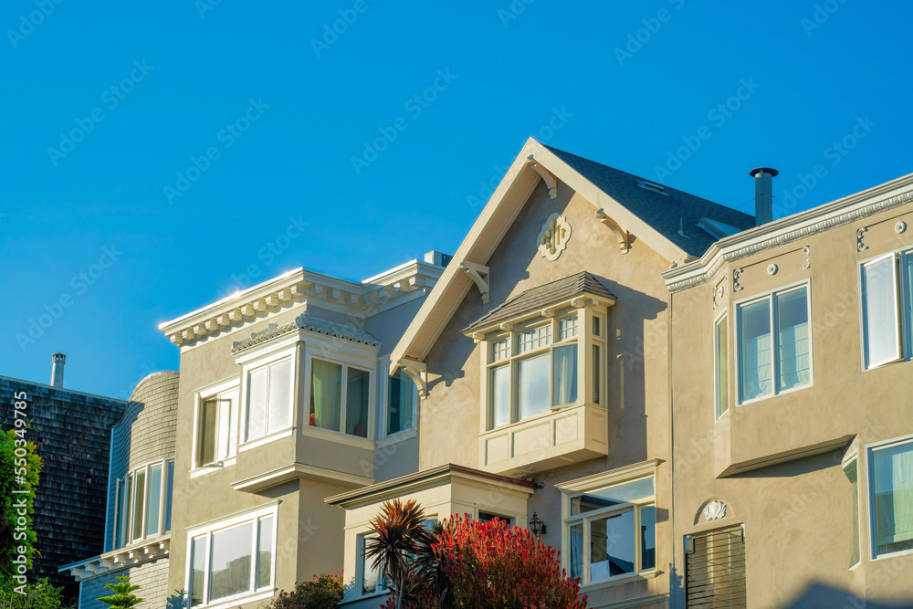 Beige stucco home or house exterior with white accent paint and clear blue gradient sky with visible roofs in late afternoon sun