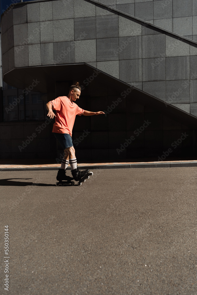 Side view of roller skater in shorts and t-shirt riding on asphalt near building outdoors.