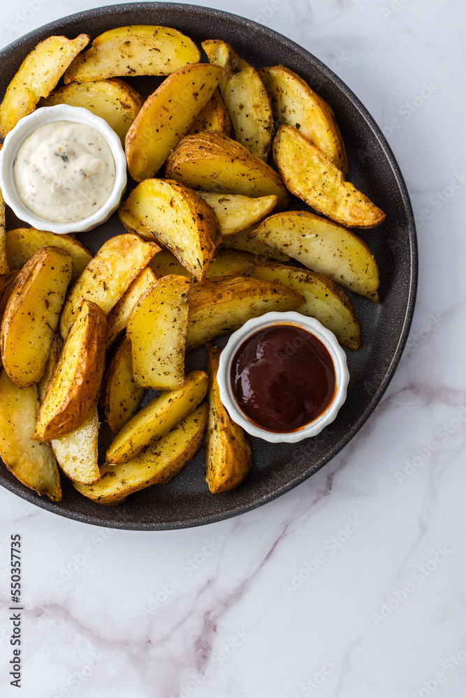 Oven roasted potatoes with skins, sliced, with sauces close-up, top view Oven roasted potatoes with skins, sliced, with sauces close-up, top view
