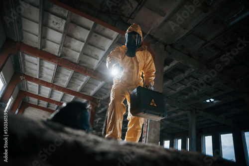 Looking below at the object. Man dressed in chemical protection suit in the ruins of the post apocalyptic building