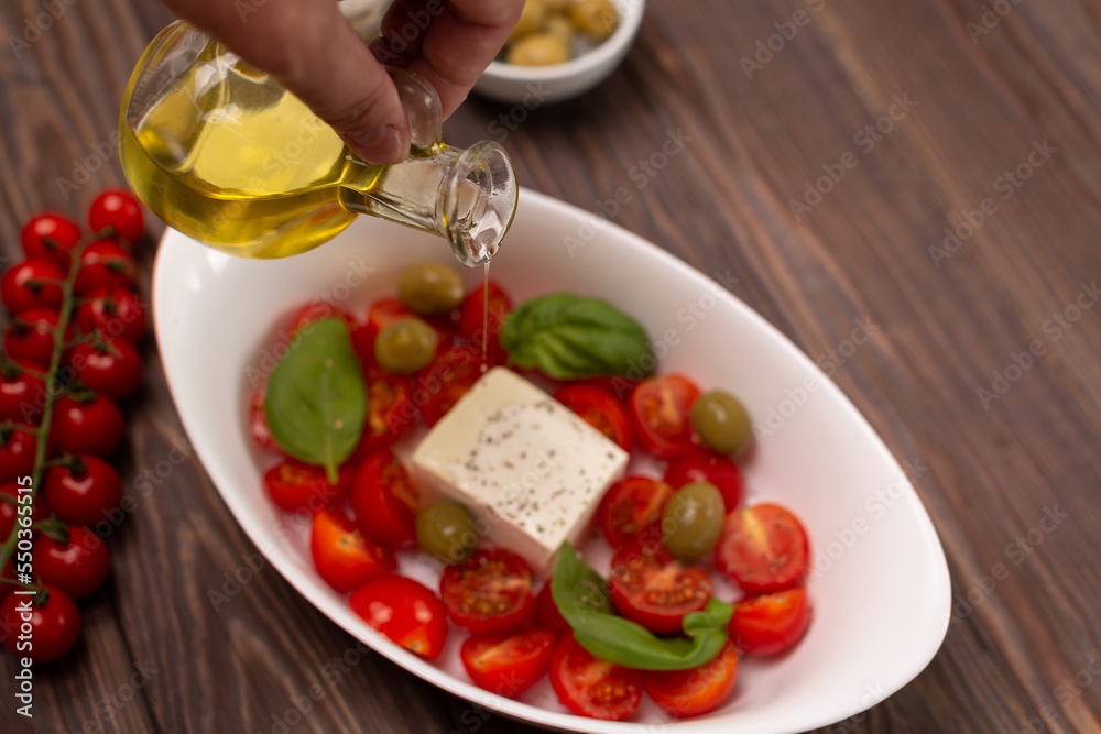 Cherry tomatoes with salted cheese, basil and olives in a deep dish prepared for baking, a man pours olive oil Cherry tomatoes with salted cheese, basil and olives in a deep dish prepared for baking, a man pours olive oil