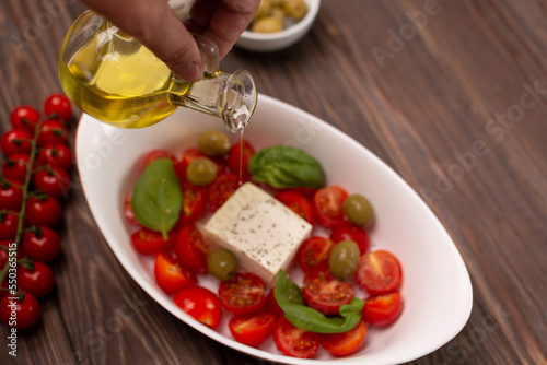 Cherry tomatoes with salted cheese  basil and olives in a deep dish prepared for baking  a man pours olive oil