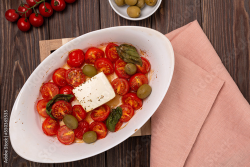 Baked cherry tomatoes with salted feta cheese, basil and olives, herbs and olive oil
