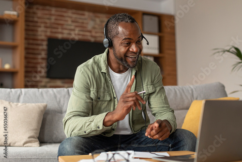 Happy busy middle aged african american male in headphones looking at laptop, gesturing