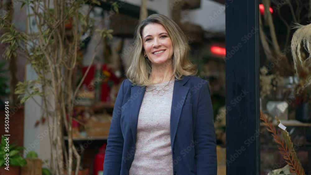 Mature woman smiling while standing in the door of her flower shop proud to be the owner of a small business Mature woman smiling while standing in the door of her flower shop proud to be the owner of a small business