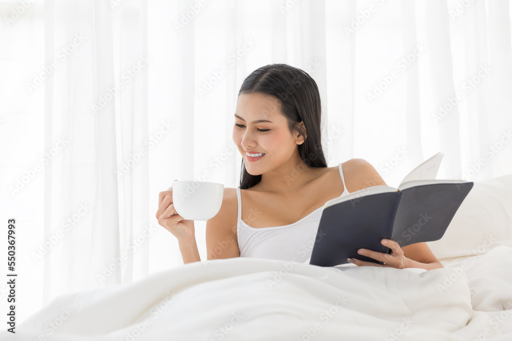 Asian young woman drinking tea and reading a book on her bed after waking up in the morning at home Asian young woman drinking tea and reading a book on her bed after waking up in the morning at home