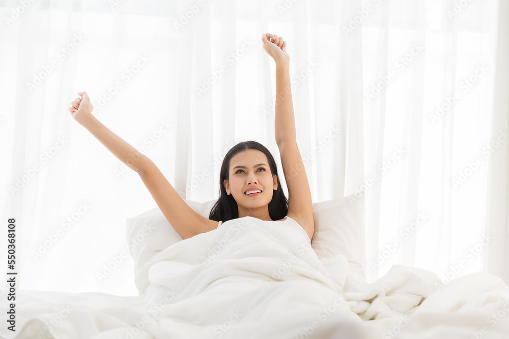 Asian young woman stretching raised arms on bed after waking up in the morning Asian young woman stretching raised arms on bed after waking up in the morning