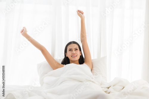 Asian young woman stretching raised arms on bed after waking up in the morning