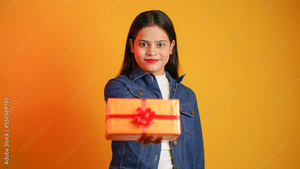 Portrait of an attractive cheerful happy girl holding gift box in hand, Young Asian Indian woman with gifts isolated over color background Portrait of an attractive cheerful happy girl holding gift box in hand, Young Asian Indian woman with gifts isolated over color background