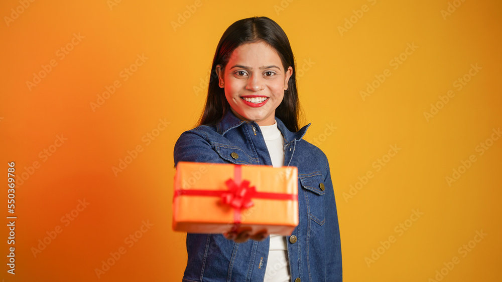 Portrait of an attractive cheerful happy girl holding gift box in hand, Young Asian Indian woman with gifts isolated over color background Portrait of an attractive cheerful happy girl holding gift box in hand, Young Asian Indian woman with gifts isolated over color background