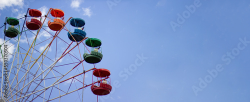 Vintage old fashioned bright multicolored Ferris wheel against a blue cloudy sky. Copy space. Banner.