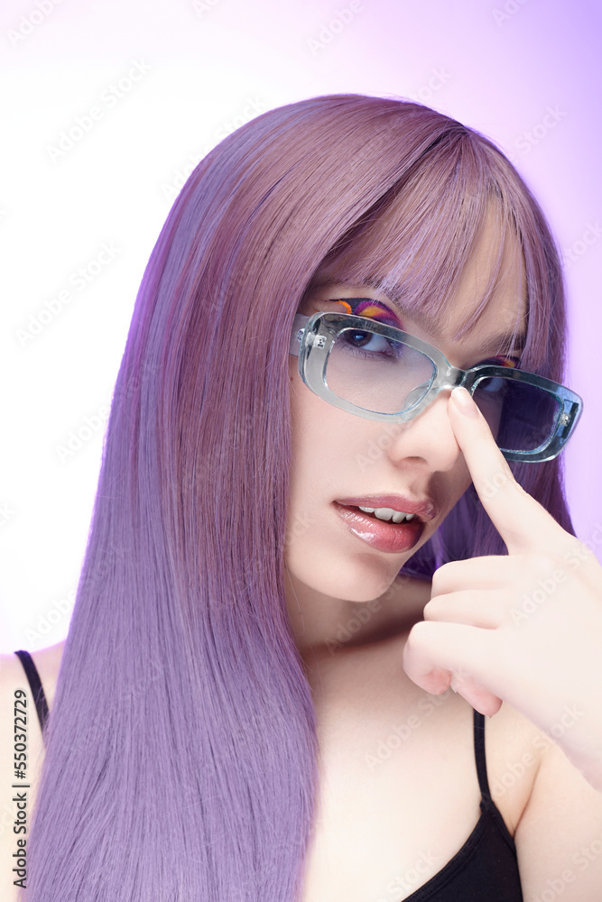 a stylish woman in a purple wig and blue glasses poses pleasantly, looking at the camera, adjusting her glasses with her hands