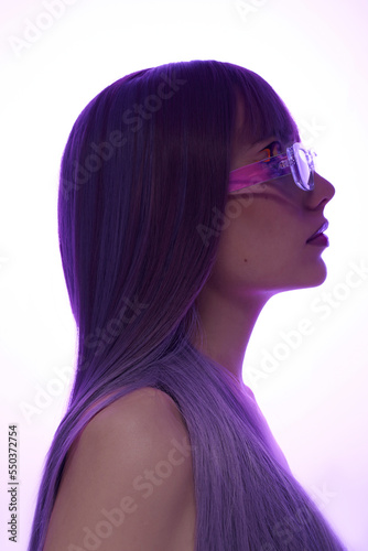 a stylish woman in a purple wig and blue glasses poses sideways to the camera in the shade