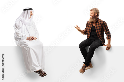 Young bearded man sitting on a blank panel and talking to an arab man