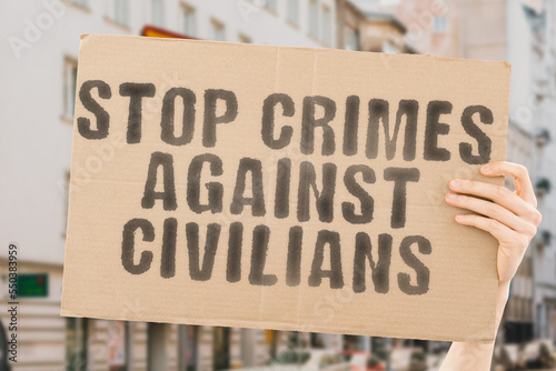 The phrase   Stop crimes against civilians   is on a banner in men s hands with blurred background. Bomb. Disaster. Explosion. Murder. Occupation. Vehicle. Chaos. People. Debris. Against. Ruin. Burnt