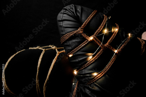 Woman with a Leg tied on a futomomo knot and a karada knot on her chest over a black velvet with lights and candle