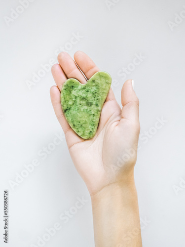 a woman holds a gua sha jade massager in her hand on a white background. home skin care, traditional skin care concept