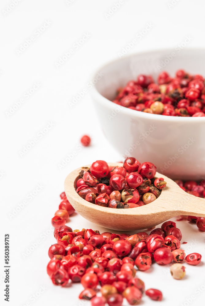 Fragrant spice pink pepper seeds in wooden spoon and a small white ceramic bowl. Close up pink peppercorn isolated Fragrant spice pink pepper seeds in wooden spoon and a small white ceramic bowl. Close up pink peppercorn isolated