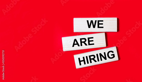 Three wooden blocks with the text WE ARE HIRING on a bright red background. Copy space