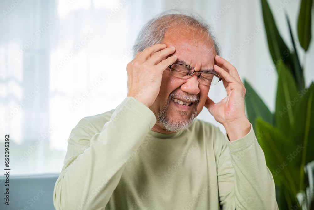 Headache. Close up of elderly holds head with hand suffering from migraine headache, Sad Asian senior man sitting on sofa feeling hurt and lonely at home, Old age health problems, healthcare Headache. Close up of elderly holds head with hand suffering from migraine headache, Sad Asian senior man sitting on sofa feeling hurt and lonely at home, Old age health problems, healthcare