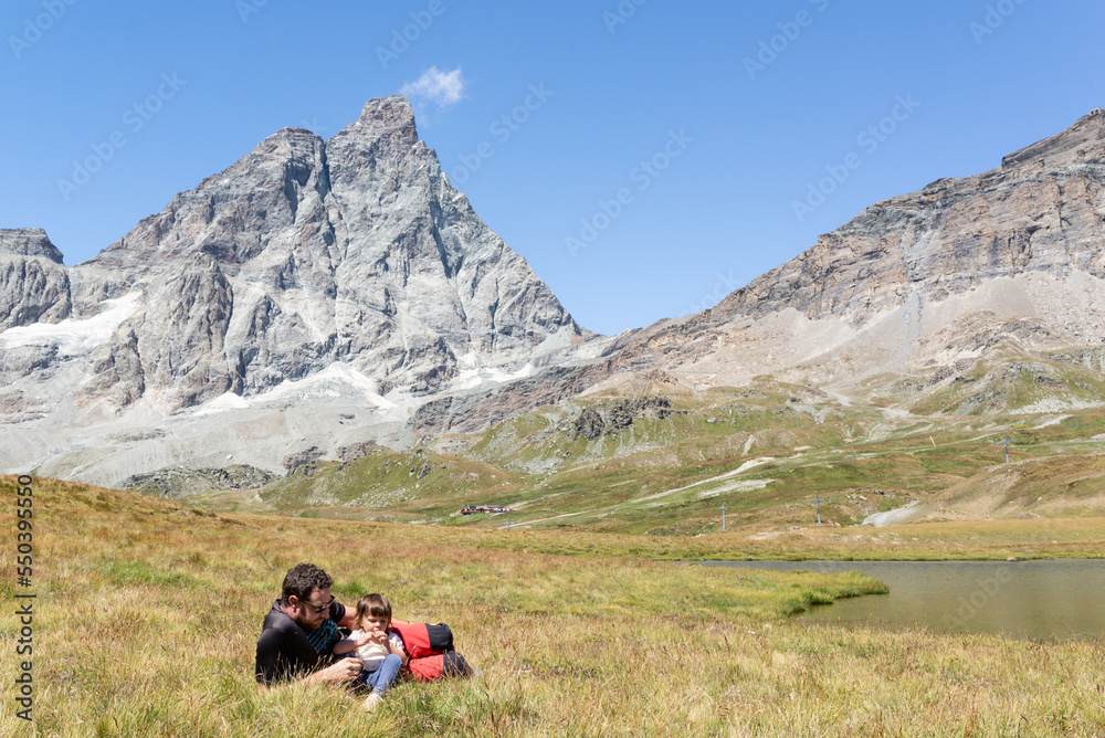Father with her little daughter lying on a meadow near a lake with views at Matterhorn at italian alps.