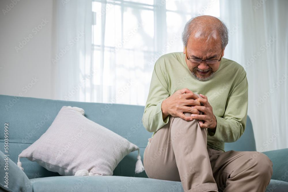 Old age. Asian senior man retirement knee joint pain on sofa, Elderly old man sitting down hands hold knee, Grandfather people health care bone problem at home