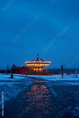 Carousel roundabout, galloper at the center an amusement park in the evening at night illumination. Outdoor vintage colorful luminous. Winter time, snow. Blue background. Copy space, vertical photo