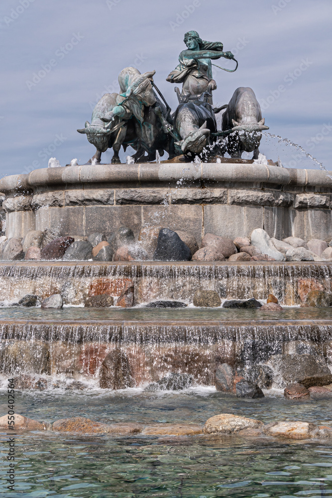 Copenhagen, Denmark - July 24, 2022: Large bronze statue composition on top of Gefion Fountain featuring oxen and the Norse goddess Gefjon against gray-blue sky. Cascade of waterfalls