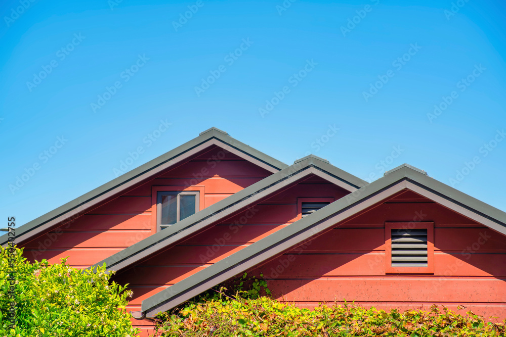 Row of double gable style roofs with red stucco exterior and dark accent paint around edges with visible insulation vents Row of double gable style roofs with red stucco exterior and dark accent paint around edges with visible insulation vents
