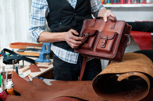 the craftsman in the workshop examines the finished leather product - a hand-made briefcase bag