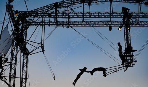 silhouettes of trapeze artists acrobats on the metal scaffolding at sunset