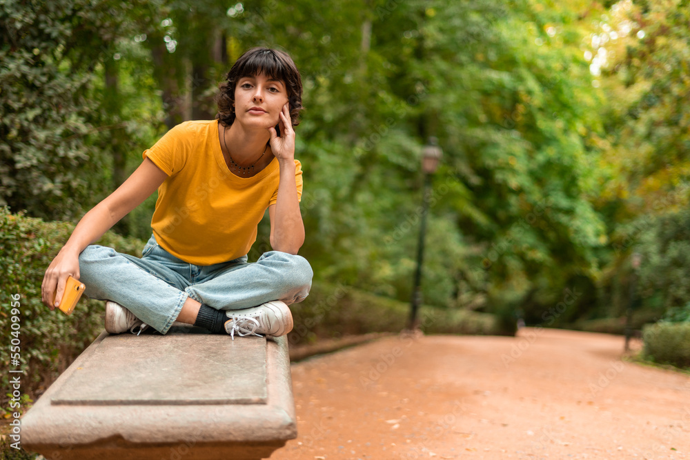 young gorgeous brunette Spanish woman sitting on a bench in the park holding her phone young gorgeous brunette Spanish woman sitting on a bench in the park holding her phone
