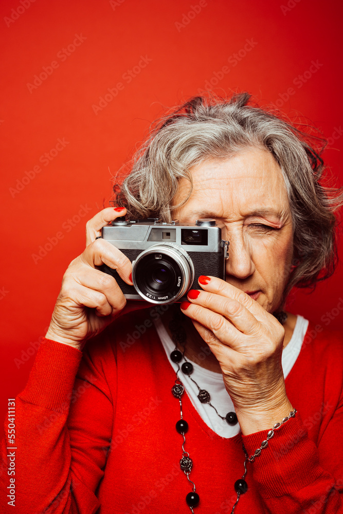Portrait of a senior woman wearing red clothes, taking pictures with an old film camera, over a red background Portrait of a senior woman wearing red clothes, taking pictures with an old film camera, over a red background