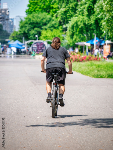 Rear view with a man in the park ridding a bicycle. Ciclyst in Youth Park (Tineretului) Bucharest, Romania.