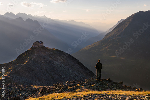 Ein Wanderer beobachtet den Sonnenuntergang über dem Gipfeln bei Sölden vor der Brunnenkogelhaus Berghütte in den Ötztaler Alpen, Österreich