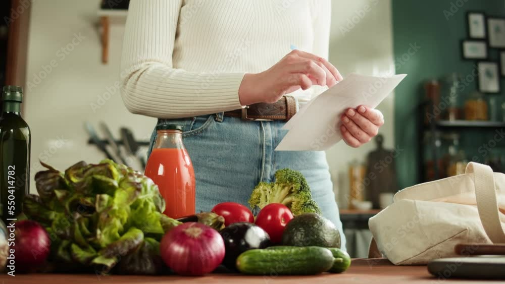 Young woman standing in kitchen and checking writing a shopping list on a notebook at home. Healthy Food on Table, Vegetable Salad recipe, Diet. Dieting Concept, Cooking At Home. Young woman standing in kitchen and checking writing a shopping list on a notebook at home. Healthy Food on Table, Vegetable Salad recipe, Diet. Dieting Concept, Cooking At Home.