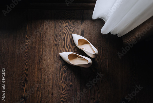 Beautiful beige shoes of the bride stand on the floor near the curtains in the room, interior. Close-up wedding photo, top view.